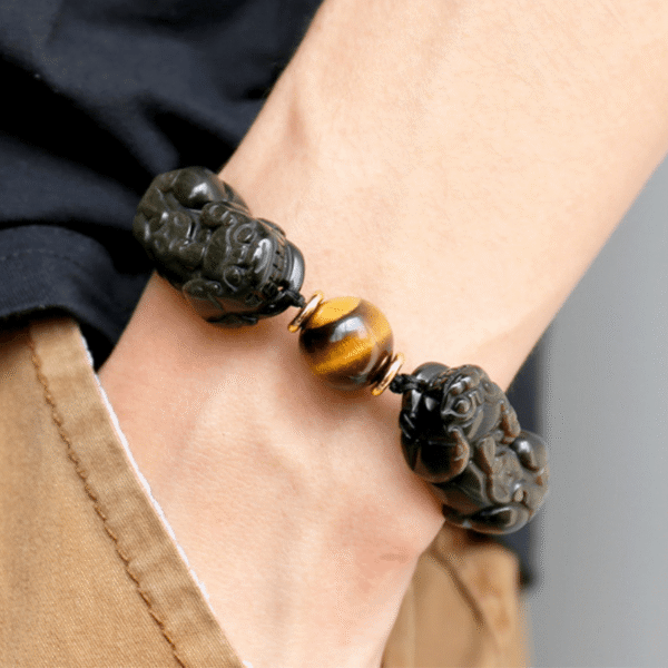 Glossy black obsidian beads with golden sheen threaded alongside two detailed metallic Pixiu charms.
