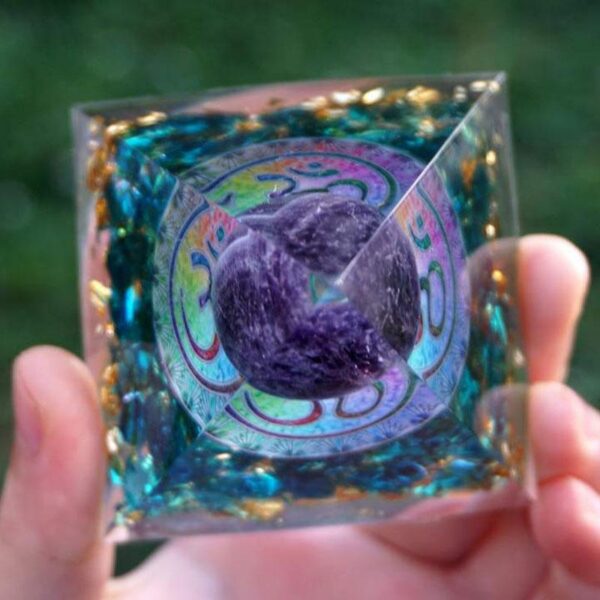 A translucent teal resin pyramid embedded with gold flakes and a central purple amethyst sphere marked with an Om symbol.