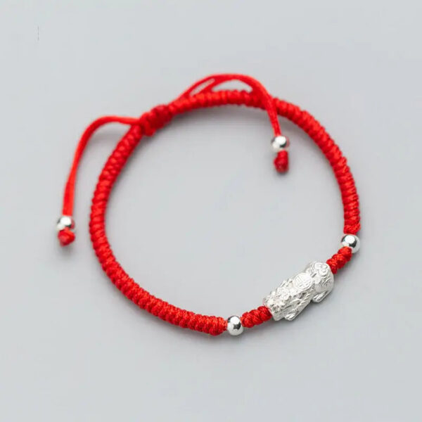 A vibrant red braided cord bracelet featuring a detailed sterling silver Pixiu charm and adjustable silver beads.