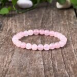 A delicate strand of smooth, translucent pink rose quartz beads resting on a rustic wooden surface with soft natural lighting.