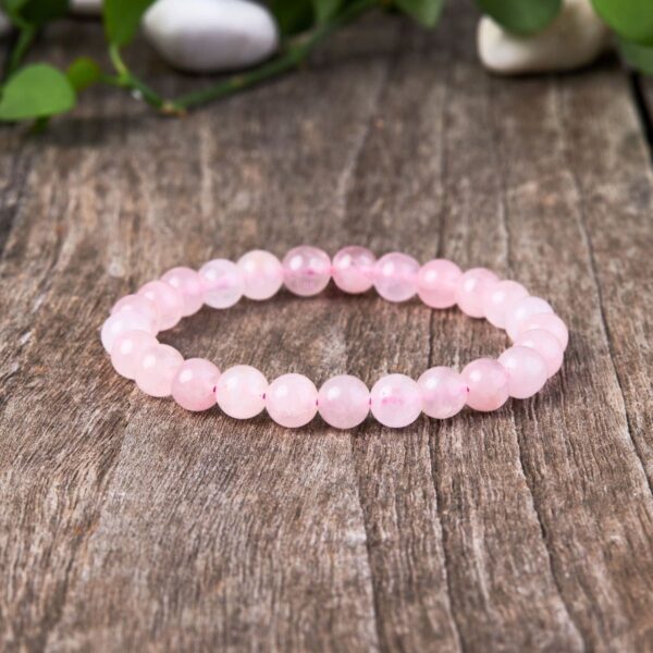 A delicate strand of smooth, translucent pink rose quartz beads resting on a rustic wooden surface with soft natural lighting.