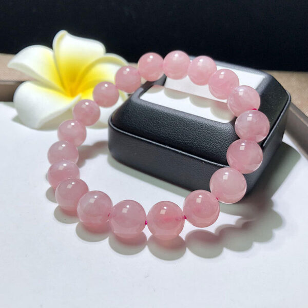 A delicate strand of smooth, translucent pink rose quartz beads resting on a rustic wooden surface with soft natural lighting.