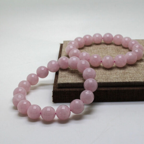 A delicate strand of smooth, translucent pink rose quartz beads resting on a rustic wooden surface with soft natural lighting.