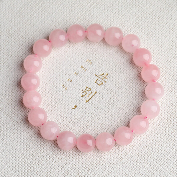 A delicate strand of smooth, translucent pink rose quartz beads resting on a rustic wooden surface with soft natural lighting.