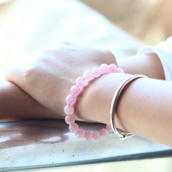 A delicate strand of smooth, translucent pink rose quartz beads resting on a rustic wooden surface with soft natural lighting.