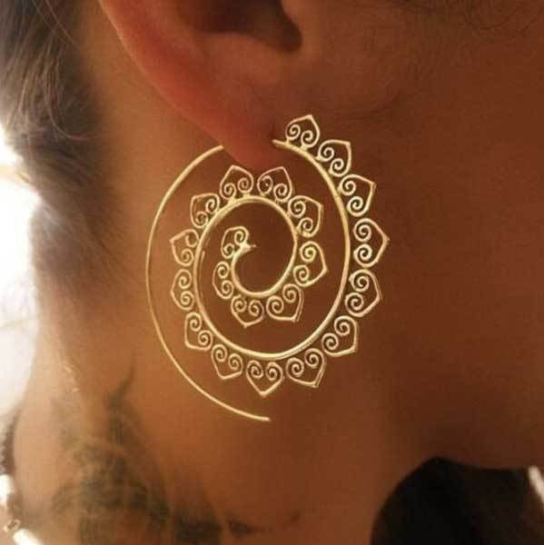 A large gold-toned wire hoop earring featuring an intricate inward spiraling pattern adorned with repeating small heart shapes.