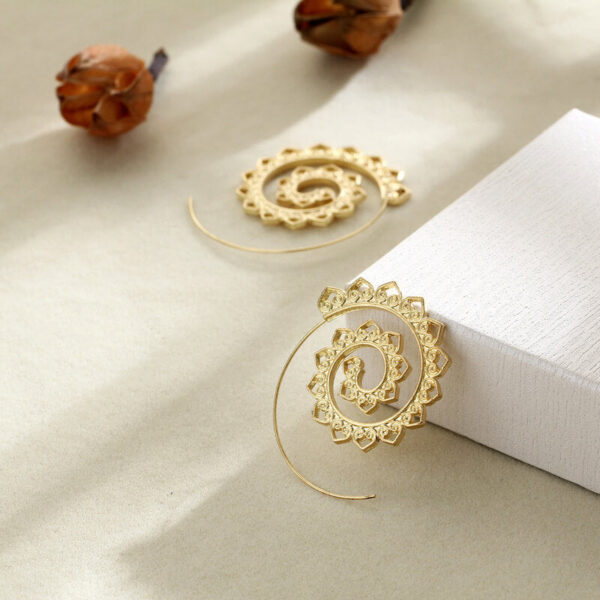 A large gold-toned wire hoop earring featuring an intricate inward spiraling pattern adorned with repeating small heart shapes.