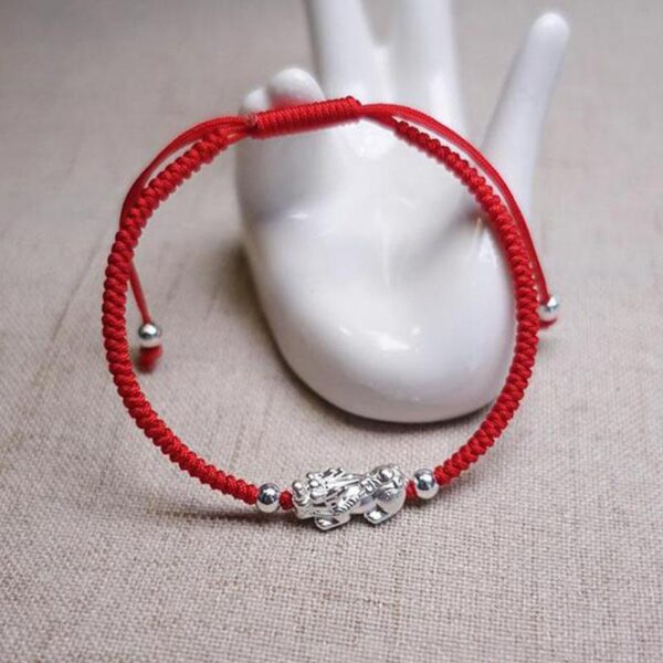 A vibrant red braided cord bracelet featuring a detailed sterling silver Pixiu charm and adjustable silver beads.