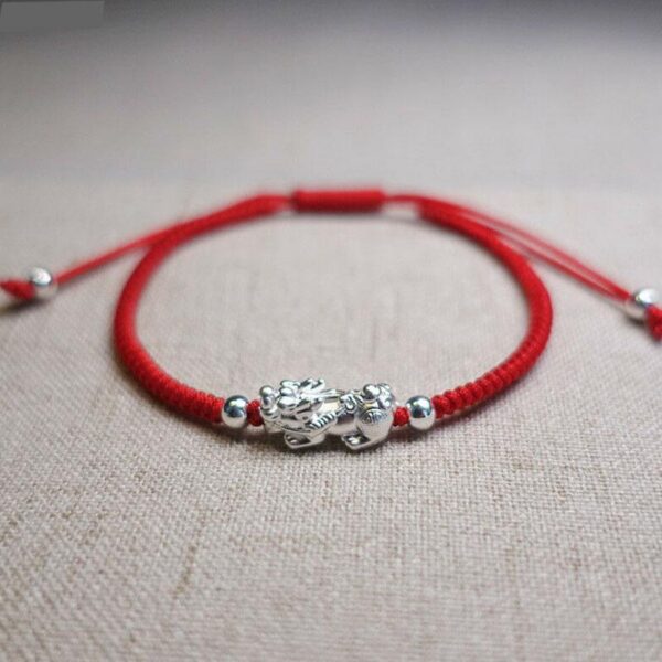 A vibrant red braided cord bracelet featuring a detailed sterling silver Pixiu charm and adjustable silver beads.