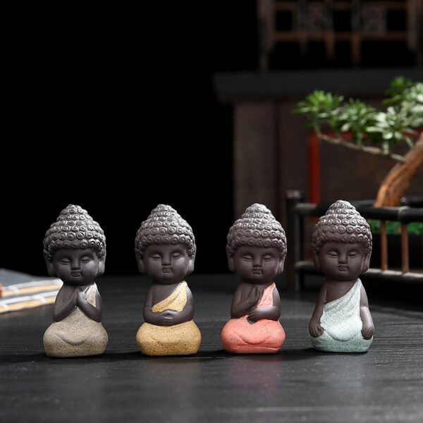 Four charming mini Buddha statues crafted from textured purple sand clay in soothing pastel shades of pink, yellow, beige, and blue.