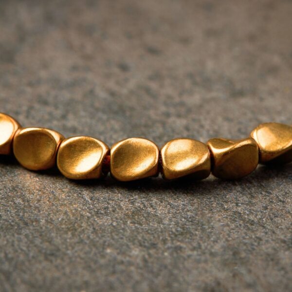 Textured gold-toned copper beads are strung on a vibrant multi-colored cord featuring traditional adjustable Tibetan sliding knots.