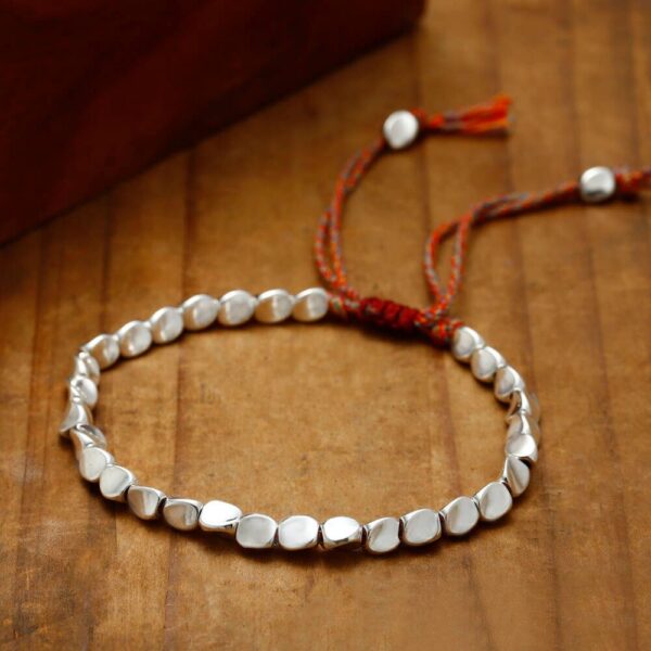 Textured gold-toned copper beads are strung on a vibrant multi-colored cord featuring traditional adjustable Tibetan sliding knots.