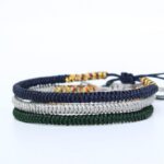 Three stacked braided cord bracelets in deep blue, silver gray, and forest green featuring adjustable Tibetan endless knots.