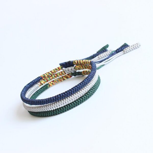 Three stacked braided cord bracelets in deep blue, silver gray, and forest green featuring adjustable Tibetan endless knots.