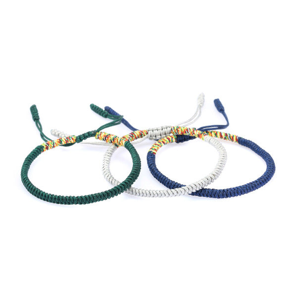 Three stacked braided cord bracelets in deep blue, silver gray, and forest green featuring adjustable Tibetan endless knots.