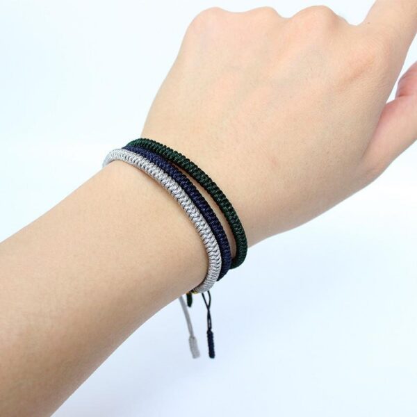 Three stacked braided cord bracelets in deep blue, silver gray, and forest green featuring adjustable Tibetan endless knots.
