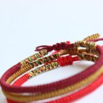 Close-up view of intricately braided cord bracelets in deep red, bright red, and golden yellow hues featuring traditional Tibetan endless knots.