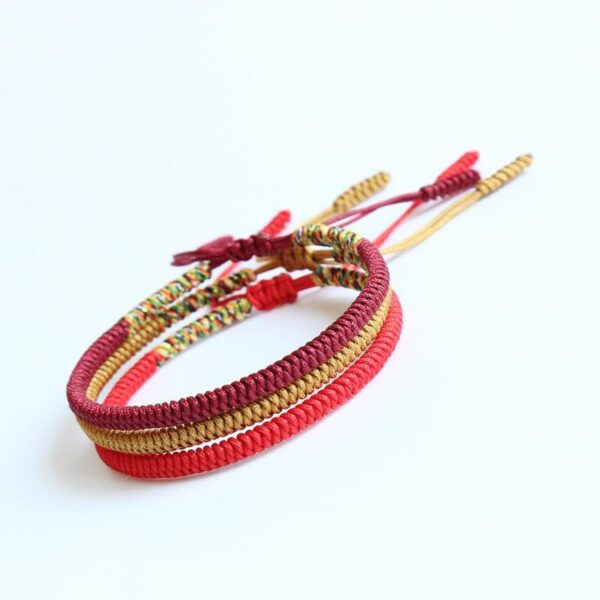 Close-up view of intricately braided cord bracelets in deep red, bright red, and golden yellow hues featuring traditional Tibetan endless knots.