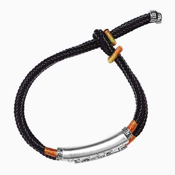 A double-strand black braided cord bracelet featuring a prominent silver cylindrical mantra bar and intricate geometric metal beads with orange gold accents.