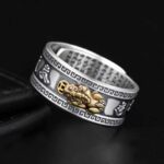 A striking silver-toned band featuring a detailed gold Pixiu creature surrounded by geometric patterns and sacred mantra engravings on the interior.